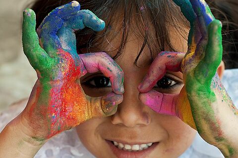 Vom Malen bunte Hände hält sich ein Kind wie eine Brille hin - Blick in die Zukunft