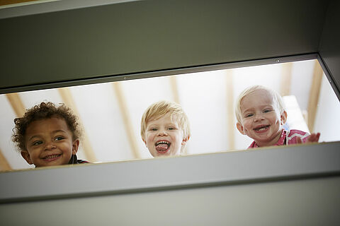 Drei lachende Kinder schauen durch das Fenster
