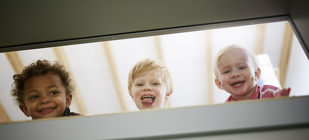 Drei lachende Kinder schauen durch das Fenster