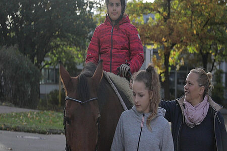 Eine Therapeuting und eine FSJlerin begleiten ein Kind auf dem Pferd - Reittherapie