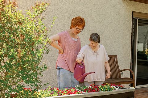 Wohnen in Gemeinschaft für Menschen mit Behinderung: Zwei Bewohnerinnen gießen Blumen in der Wohnstätte.