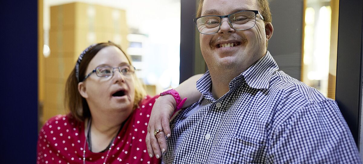 Berufliche Bildung für Menschen mit Behinderung. Eine Klientin und ein Klient lachen in die Kamera.