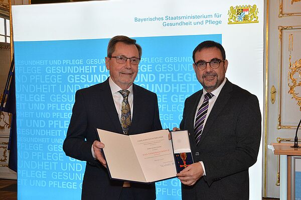 Minister Holateschek übergibt Rudolf Bader das Bundesverdienstkreuz und die Urkunde.